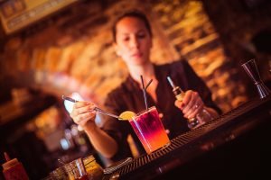 Midsection of a young female bartender preparing a cocktail in a nightlife cocktail bar. Selective focus. Focus on foreground.